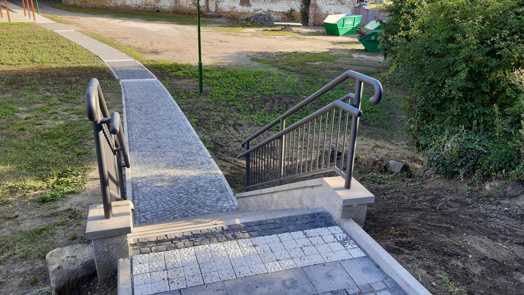 Zábradlí lakované I — antracitové trubkové zábradlí navazující na chodník s kostkovou dlažbou a slepeckou signální plochou