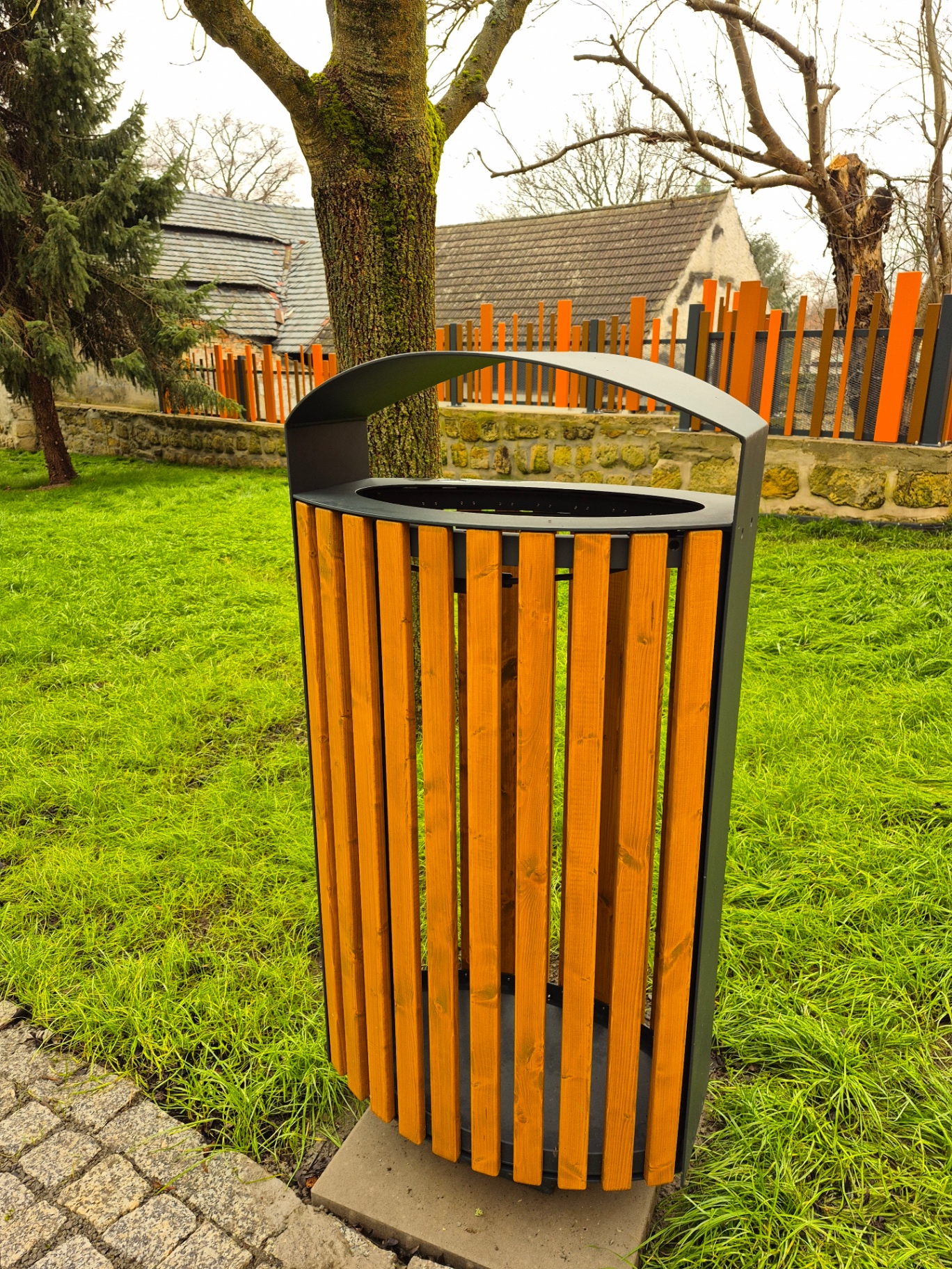 Městský mobiliář — oválný odpadkový koš s dřevěnými latěmi v parku