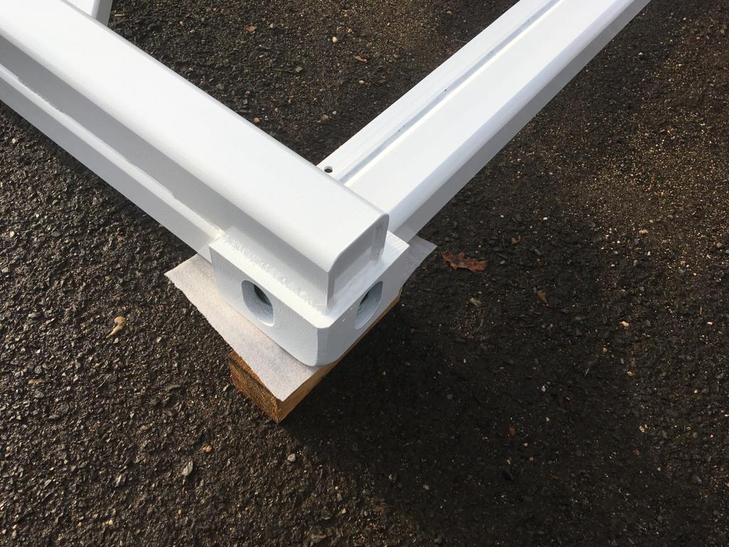 Ocelový rám — detail rohové patky s montážními otvory a bílou vypalovací barvou