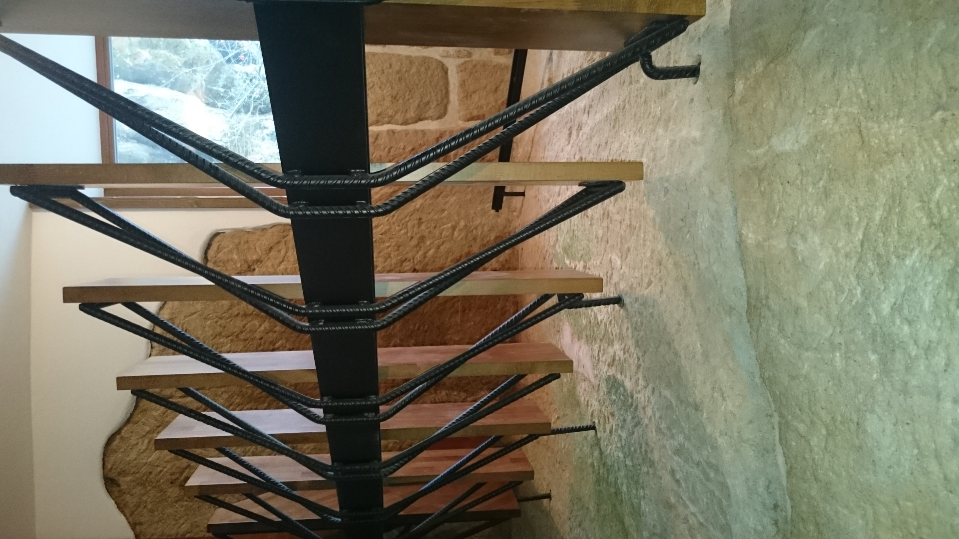 Schodiště lakované IV — detail nosného černého sloupu, dřevěných stupňů a výplně z ohýbané betonářské oceli