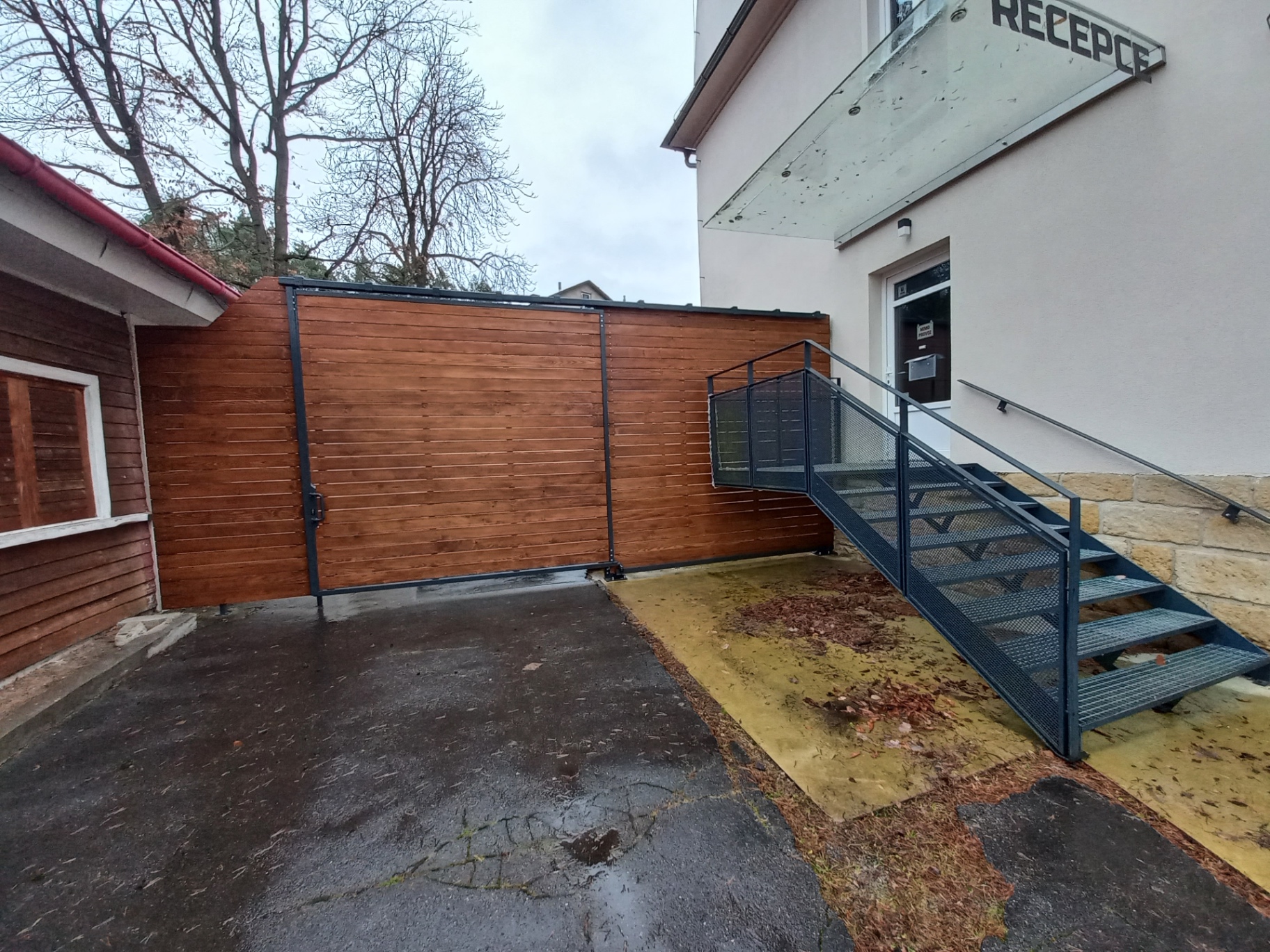 Závěsná vrata s dřevěnou výplní — celkový pohled na vrata s antracitovým rámem vedle ocelového schodiště k recepci